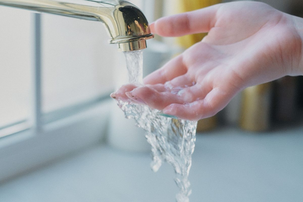 Perfectly clear water running from a household tap over an open hand into a white sink.