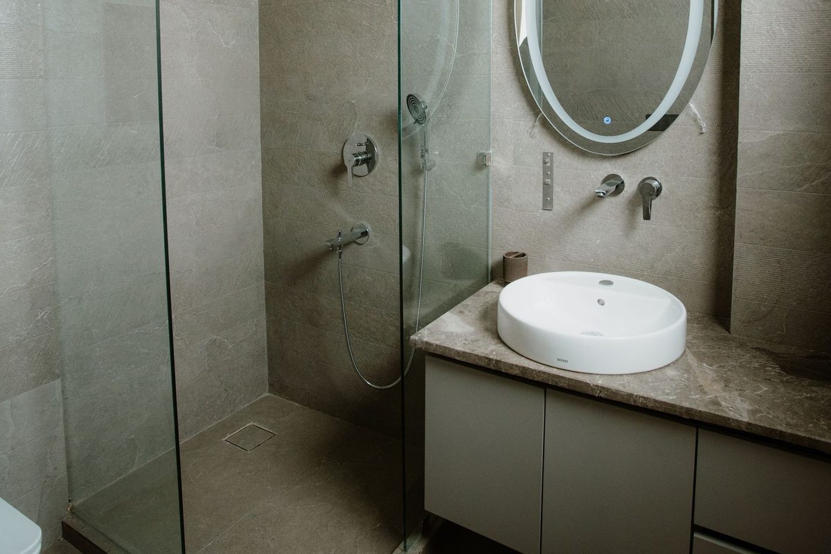 A condo bathroom with a glass shower stall, wall-mounted shower valves, a vessel sink and a wall faucet above a stone vanity.