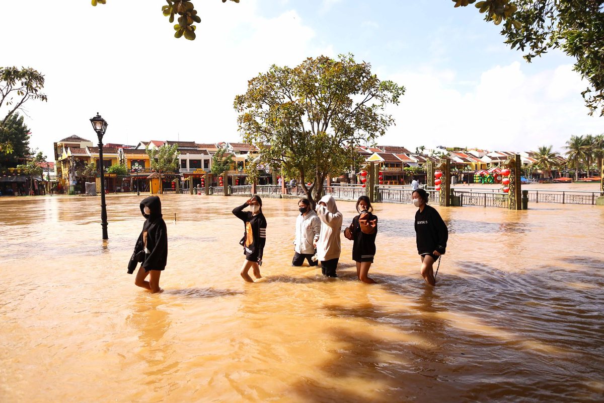 Residents wading through knee-deep brown floodwater in a Southeast Asian town as the water starts to recede under a clearing sky.