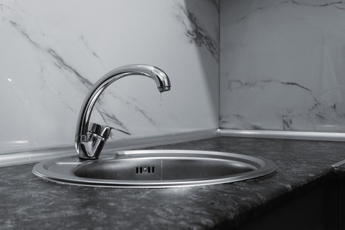 A chrome kitchen faucet over a round steel sink with a thin stream of water still dripping from the spout.
