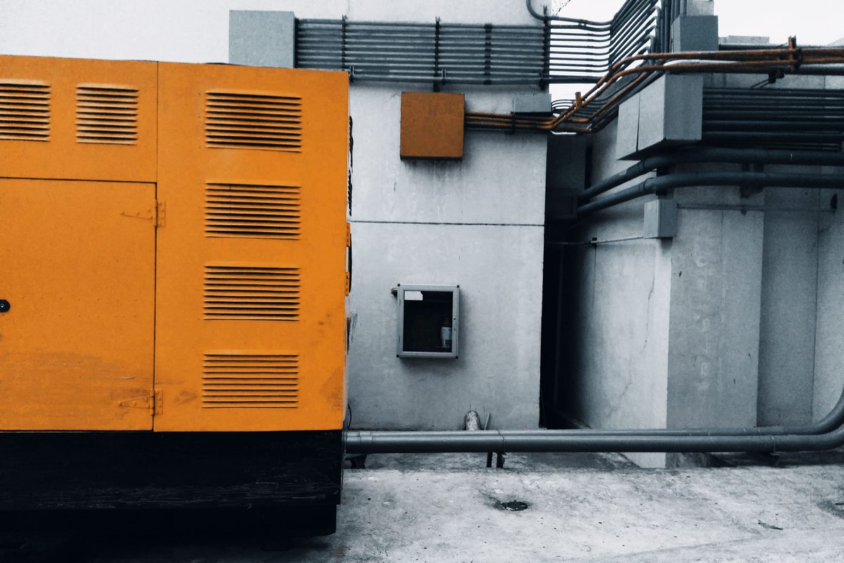 Yellow canopy standby generator installed outdoors on a concrete pad against a building wall lined with electrical conduit.