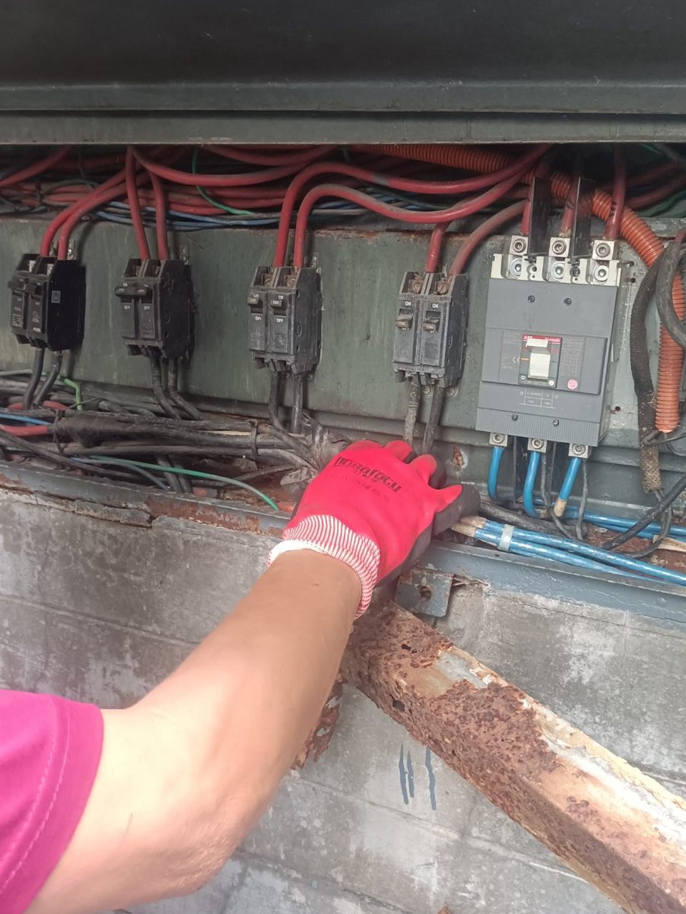 A KuyaYos electrician in gloves repairing a shorted breaker in an outdoor panel