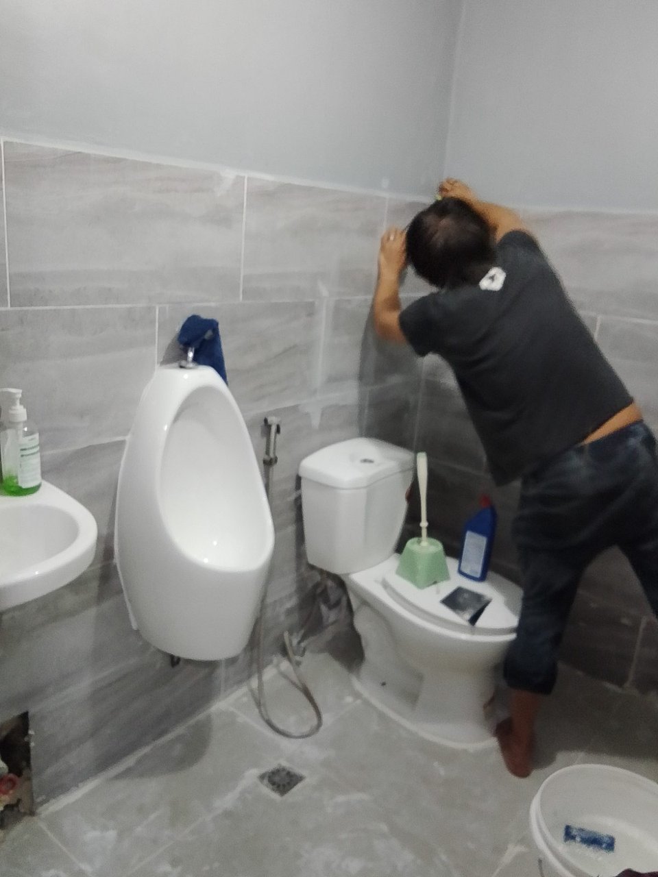 A KuyaYos mason finishing the wall tiles of a bathroom